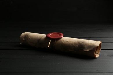 Photo of One old rolled scroll with wax seal on black wooden table, closeup