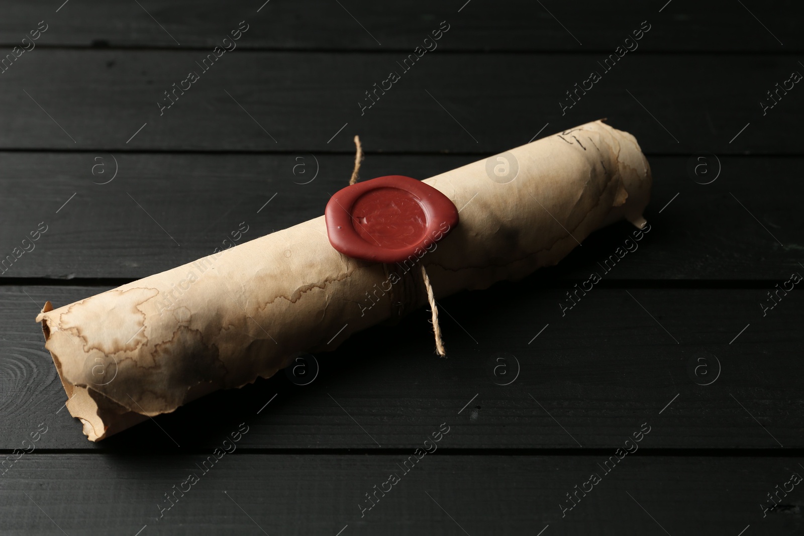 One old rolled scroll with wax seal on black wooden table, closeup Photo of One old rolled scroll with wax seal on black wooden table, closeup