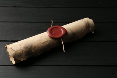 Photo of One old rolled scroll with wax seal on black wooden table, closeup