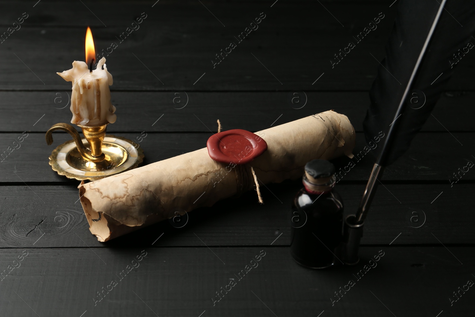 Old rolled scroll, feather, inkwell and burning candle on black wooden table, closeup Photo of Old rolled scroll, feather, inkwell and burning candle on black wooden table, closeup