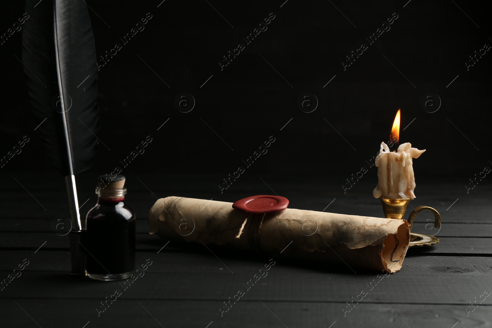 Old rolled scroll, feather, inkwell and burning candle on black wooden table, closeup Photo of Old rolled scroll, feather, inkwell and burning candle on black wooden table, closeup