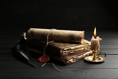 Photo of Old rolled scroll, burning candle, feather and books on black wooden table