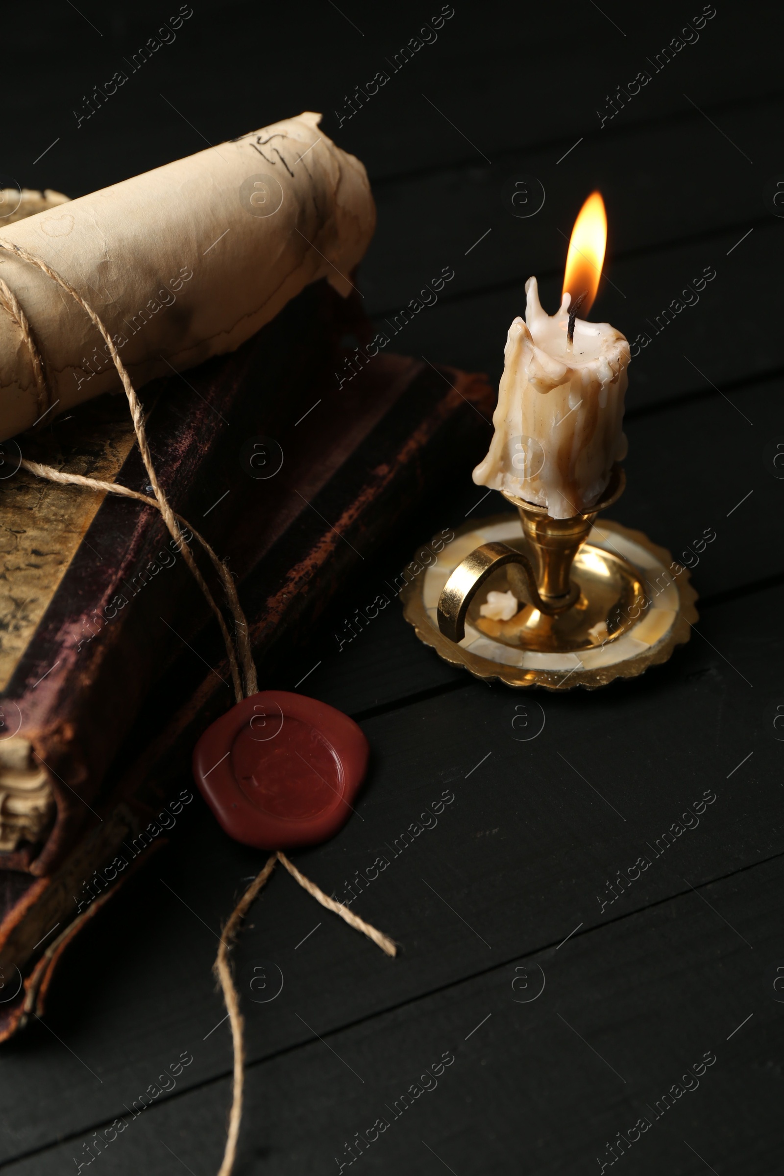 Old rolled scroll, burning candle and books on black wooden table, closeup Photo of Old rolled scroll, burning candle and books on black wooden table, closeup