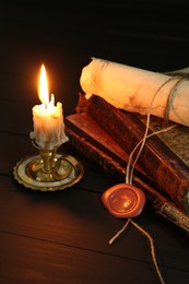 Photo of Old rolled scroll, burning candle and books on black wooden table, closeup