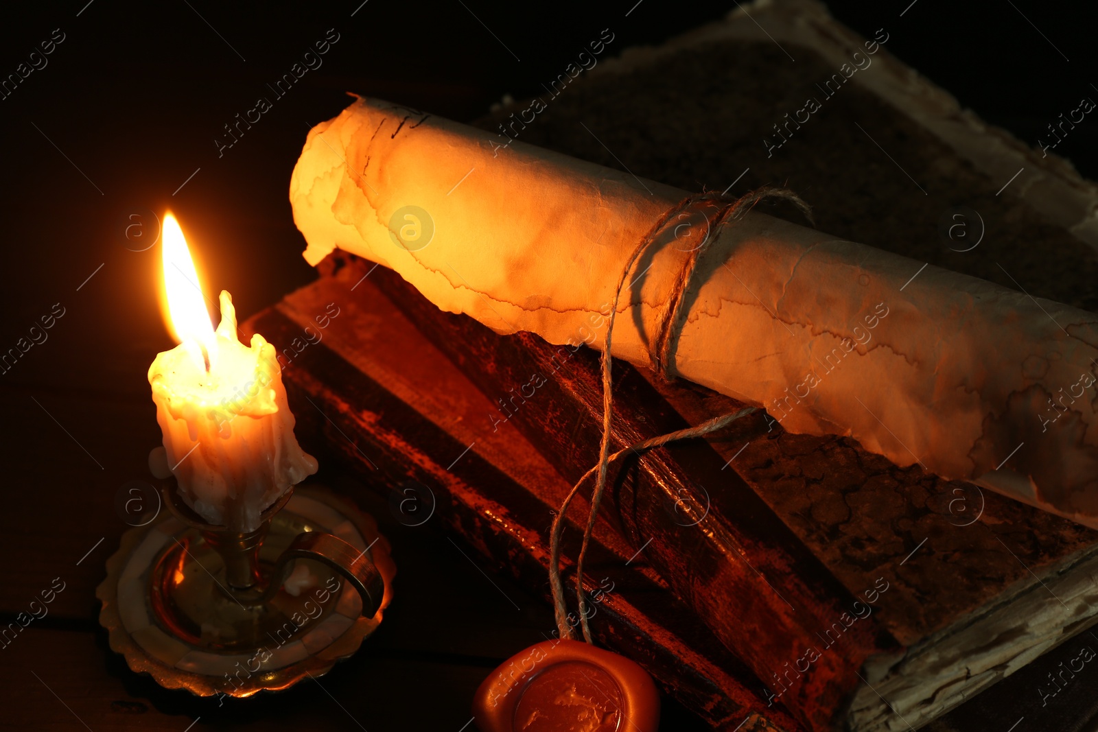 Old rolled scroll, burning candle and books on black wooden table, closeup Photo of Old rolled scroll, burning candle and books on black wooden table, closeup