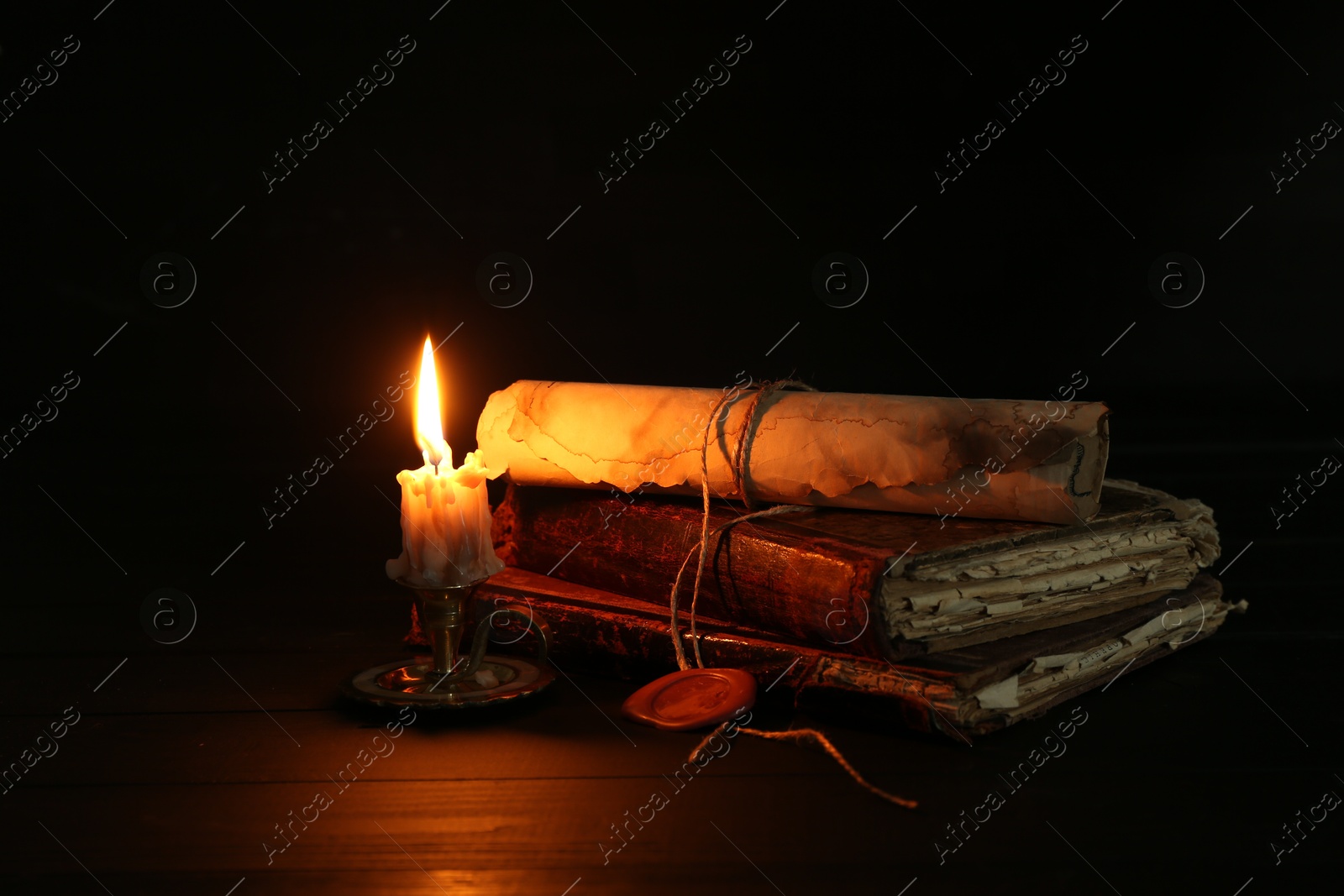 Old rolled scroll, burning candle and books on black wooden table, closeup Photo of Old rolled scroll, burning candle and books on black wooden table, closeup