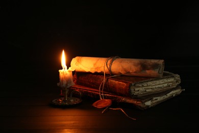 Photo of Old rolled scroll, burning candle and books on black wooden table, closeup