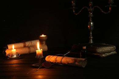 Photo of Many old rolled scrolls and burning candles on black wooden table, closeup