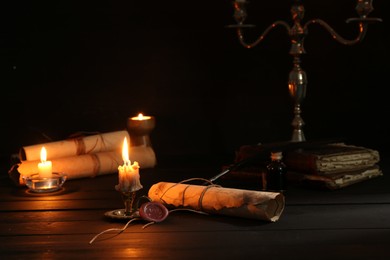 Photo of Many old rolled scrolls and burning candles on black wooden table, closeup