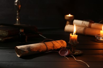 Photo of Many old rolled scrolls and burning candles on black wooden table, closeup