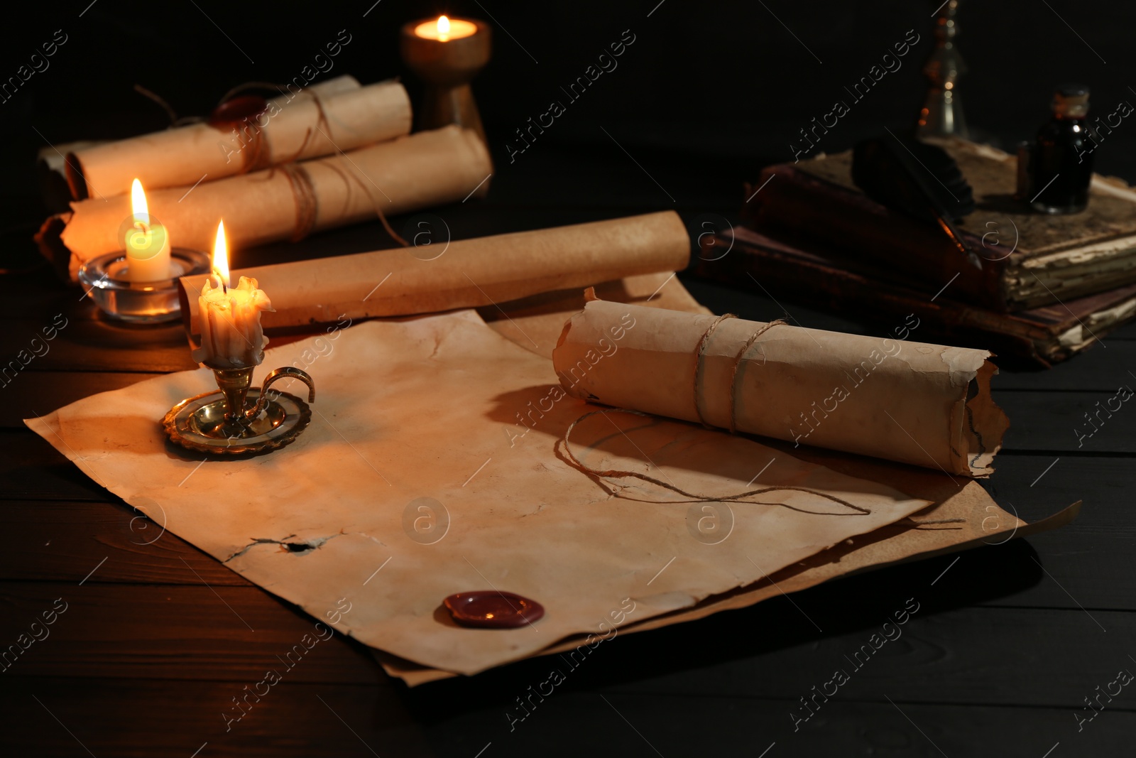 Many old rolled scrolls, burning candles and books on black wooden table, closeup Photo of Many old rolled scrolls, burning candles and books on black wooden table, closeup