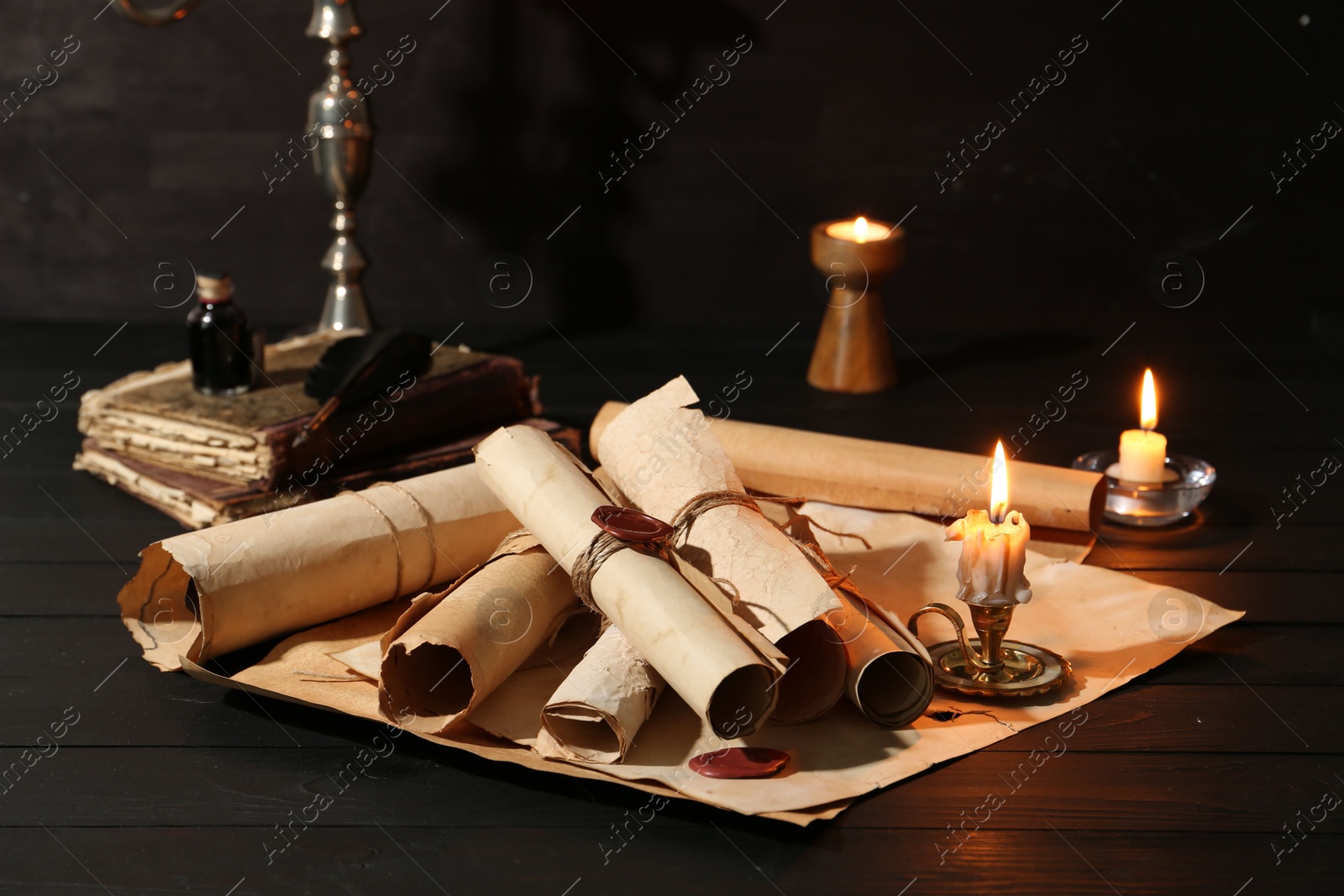 Many old rolled scrolls, burning candles and books on black wooden table, closeup Photo of Many old rolled scrolls, burning candles and books on black wooden table, closeup