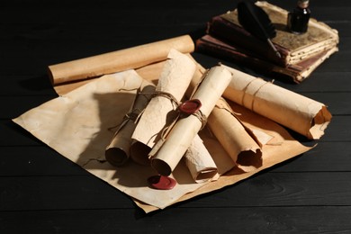 Photo of Many old rolled scrolls and books on black wooden table, closeup