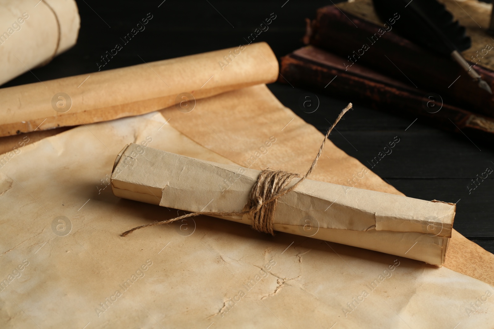 Many old rolled scrolls and books on black wooden table, closeup Photo of Many old rolled scrolls and books on black wooden table, closeup
