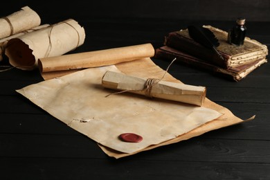 Photo of Many old rolled scrolls and books on black wooden table, closeup