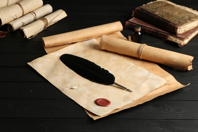 Photo of Many old rolled scrolls, feather and inkwell on black wooden table, closeup