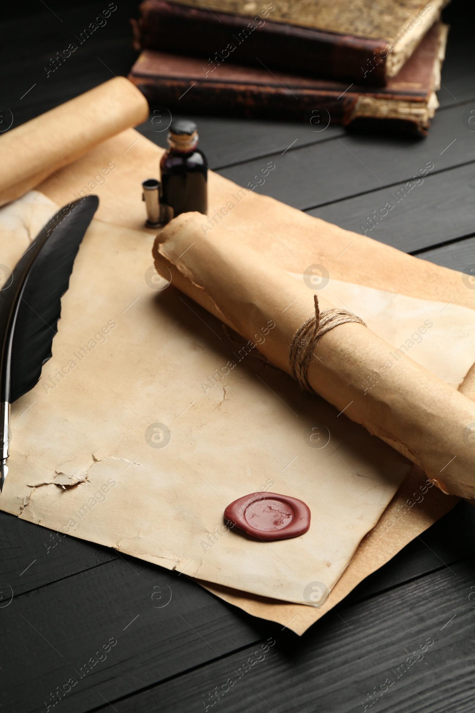 Many old rolled scrolls, feather and inkwell on black wooden table, closeup Photo of Many old rolled scrolls, feather and inkwell on black wooden table, closeup