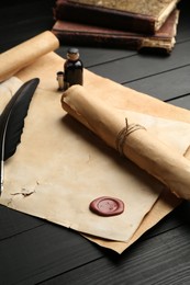 Photo of Many old rolled scrolls, feather and inkwell on black wooden table, closeup