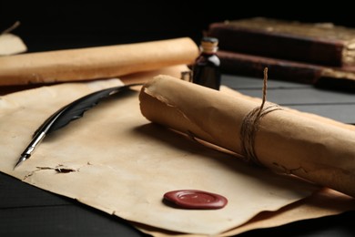 Photo of Many old rolled scrolls, feather and inkwell on black wooden table, closeup