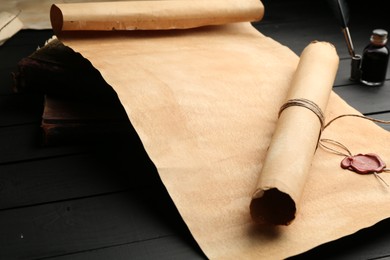 Photo of Old rolled scrolls and books on black wooden table, closeup