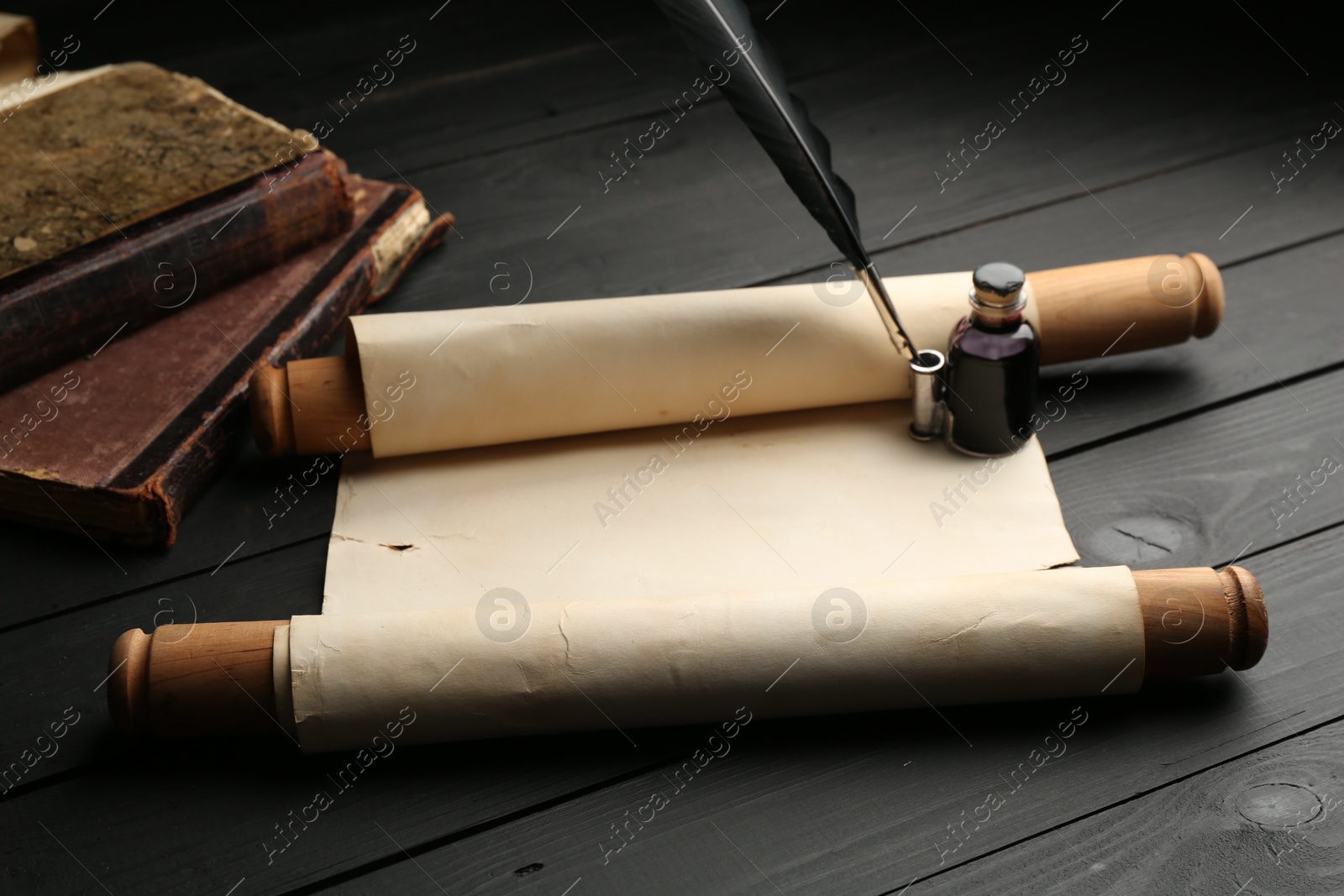 Old rolled scroll, books, feather and inkwell on black wooden table Photo of Old rolled scroll, books, feather and inkwell on black wooden table