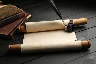 Photo of Old rolled scroll, books, feather and inkwell on black wooden table