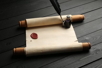 Photo of Old rolled scroll, feather and inkwell on black wooden table