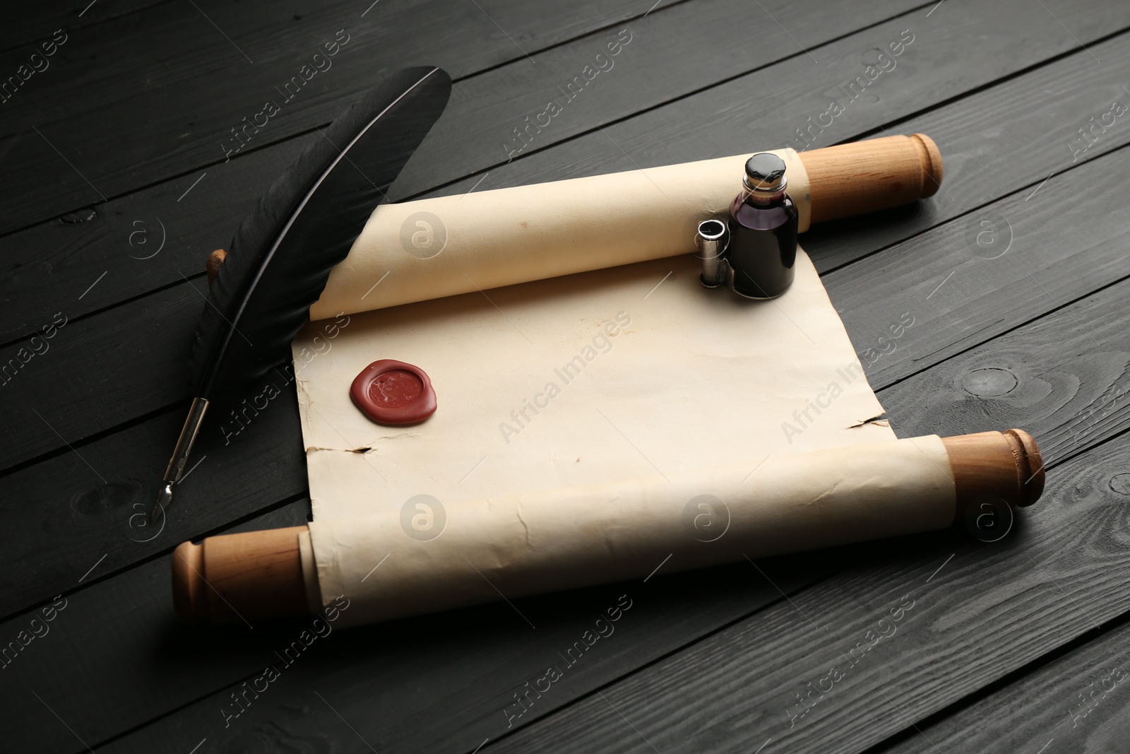 Old rolled scroll, feather and inkwell on black wooden table Photo of Old rolled scroll, feather and inkwell on black wooden table