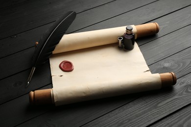Photo of Old rolled scroll, feather and inkwell on black wooden table