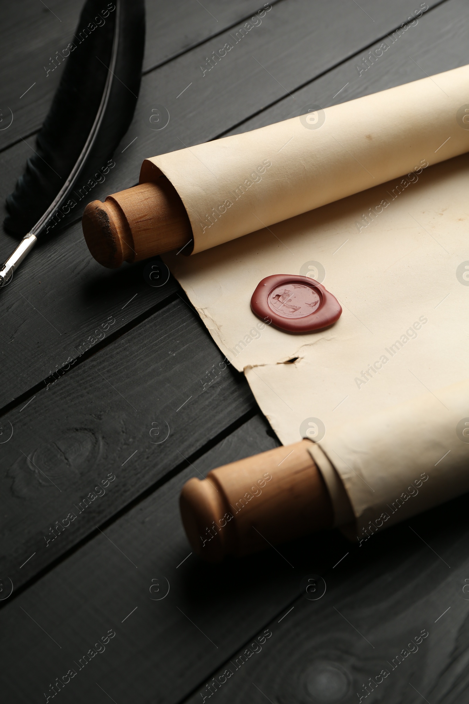 Old rolled scroll and feather on black wooden table, closeup Photo of Old rolled scroll and feather on black wooden table, closeup