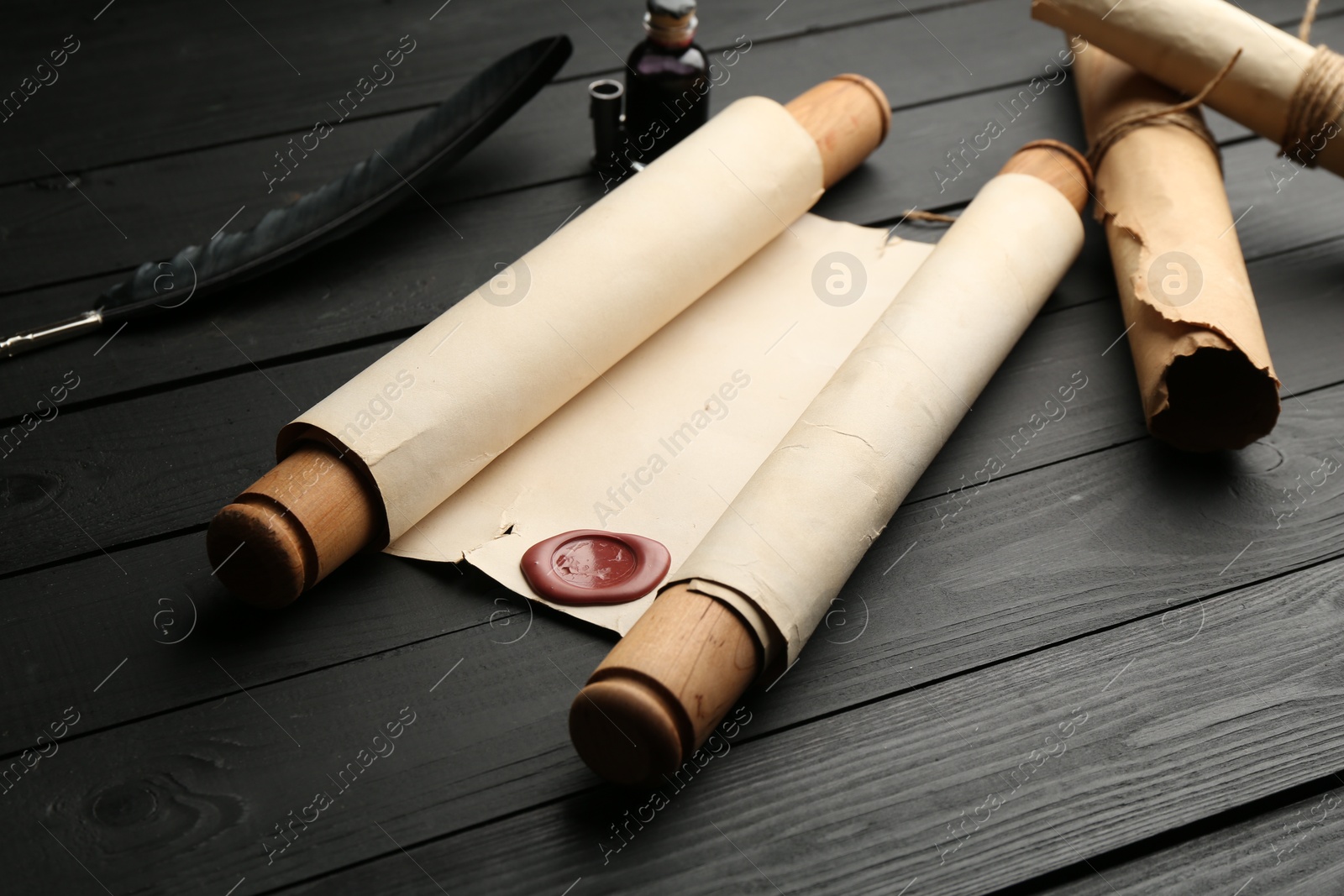Many old rolled scrolls, feather and inkwell on black wooden table, closeup Photo of Many old rolled scrolls, feather and inkwell on black wooden table, closeup