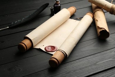 Photo of Many old rolled scrolls, feather and inkwell on black wooden table, closeup