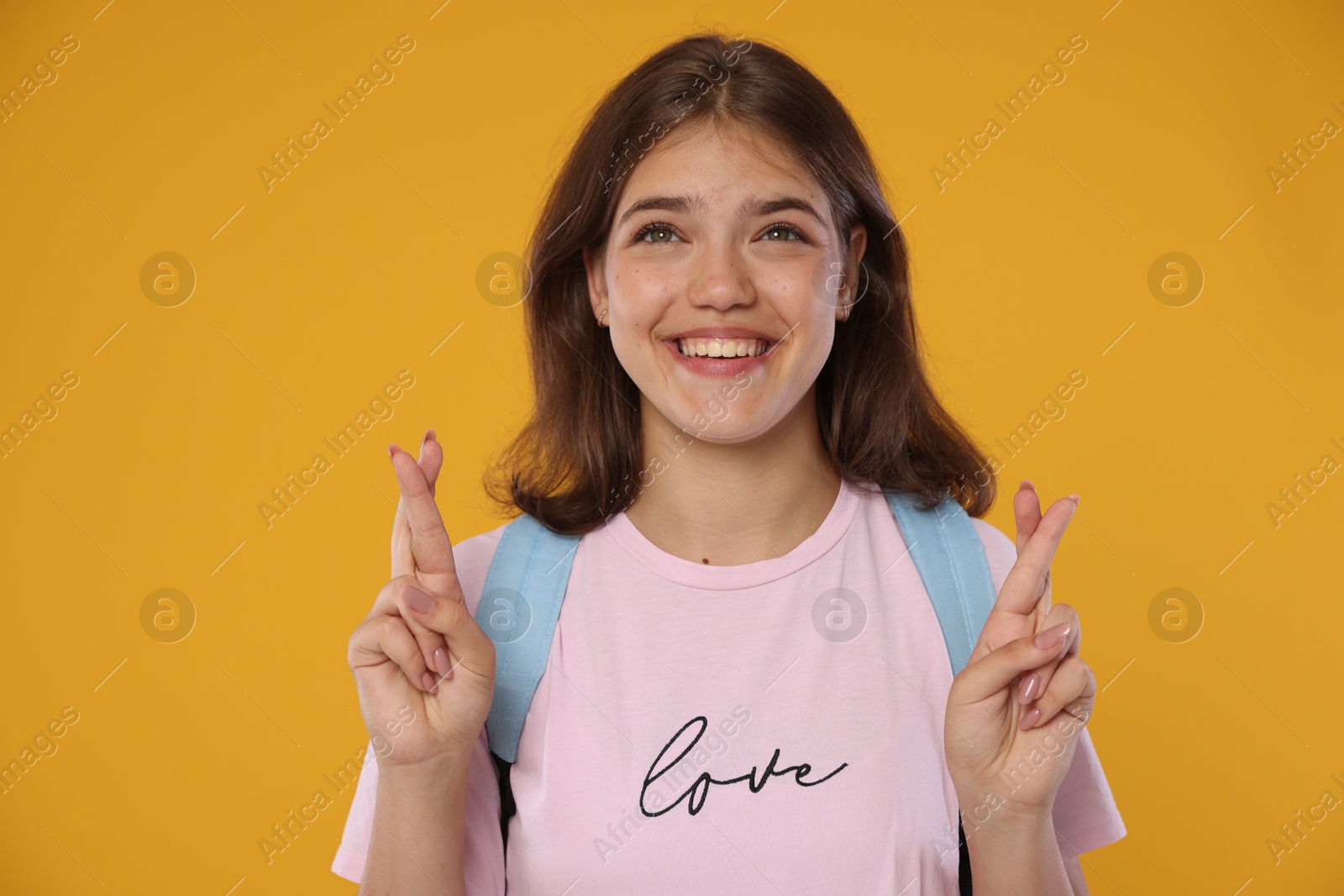 Excited student crossing fingers on orange background. Hope for good exam result Photo of Excited student crossing fingers on orange background. Hope for good exam result