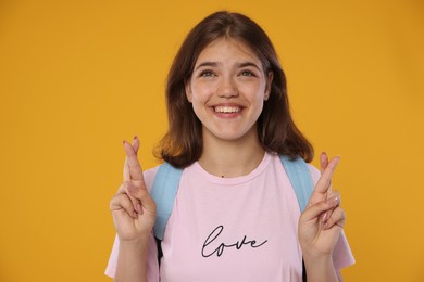 Photo of Excited student crossing fingers on orange background. Hope for good exam result