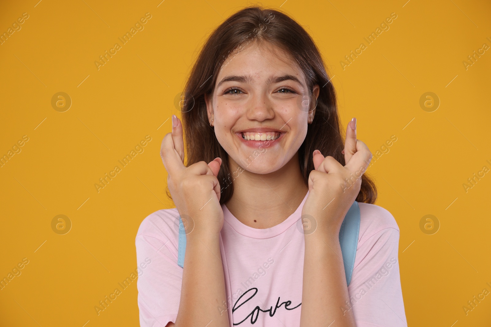 Excited student crossing fingers on orange background. Hope for good exam result Photo of Excited student crossing fingers on orange background. Hope for good exam result