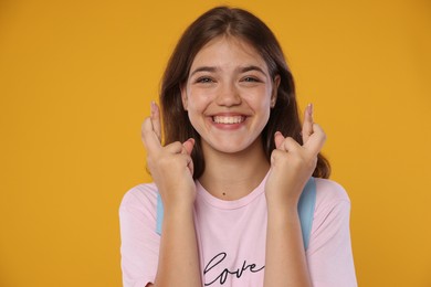 Photo of Excited student crossing fingers on orange background. Hope for good exam result