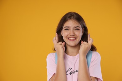 Photo of Excited student crossing fingers on orange background. Hope for good exam result