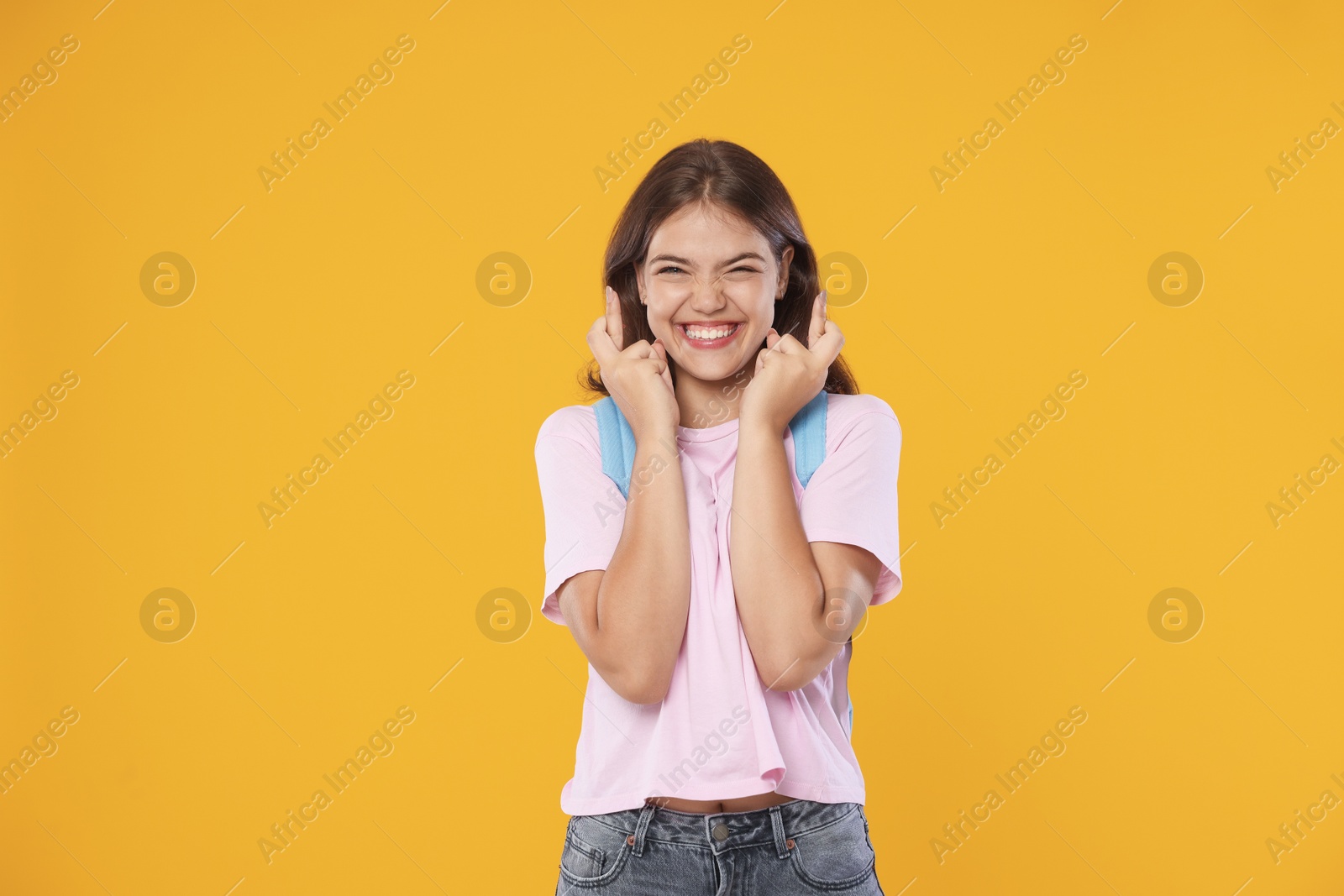 Excited student crossing fingers on orange background. Hope for good exam result Photo of Excited student crossing fingers on orange background. Hope for good exam result