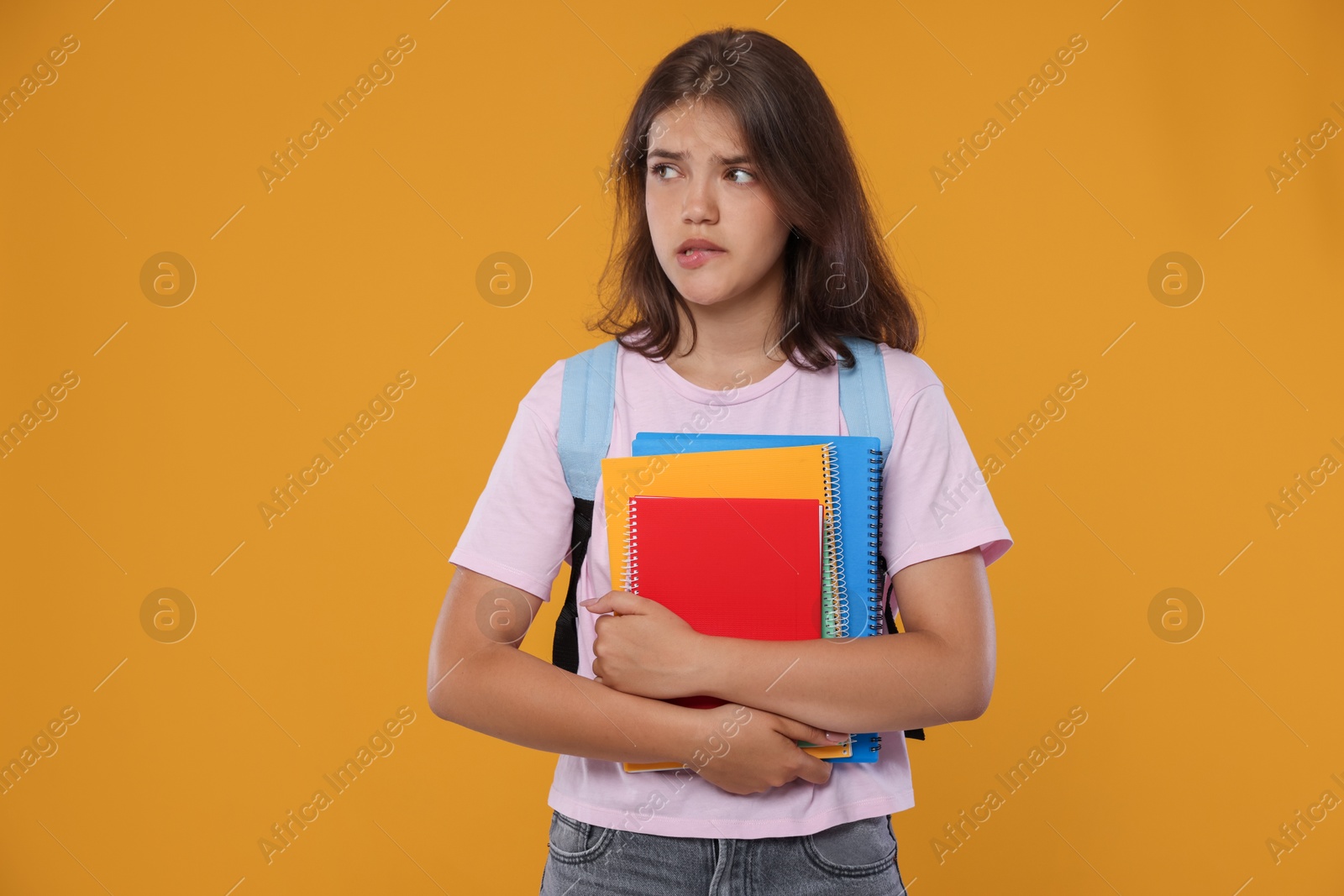 Student with notebooks worried about her exam result on orange background Photo of Student with notebooks worried about her exam result on orange background