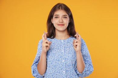 Photo of Student crossing fingers on orange background. Hope for good exam result