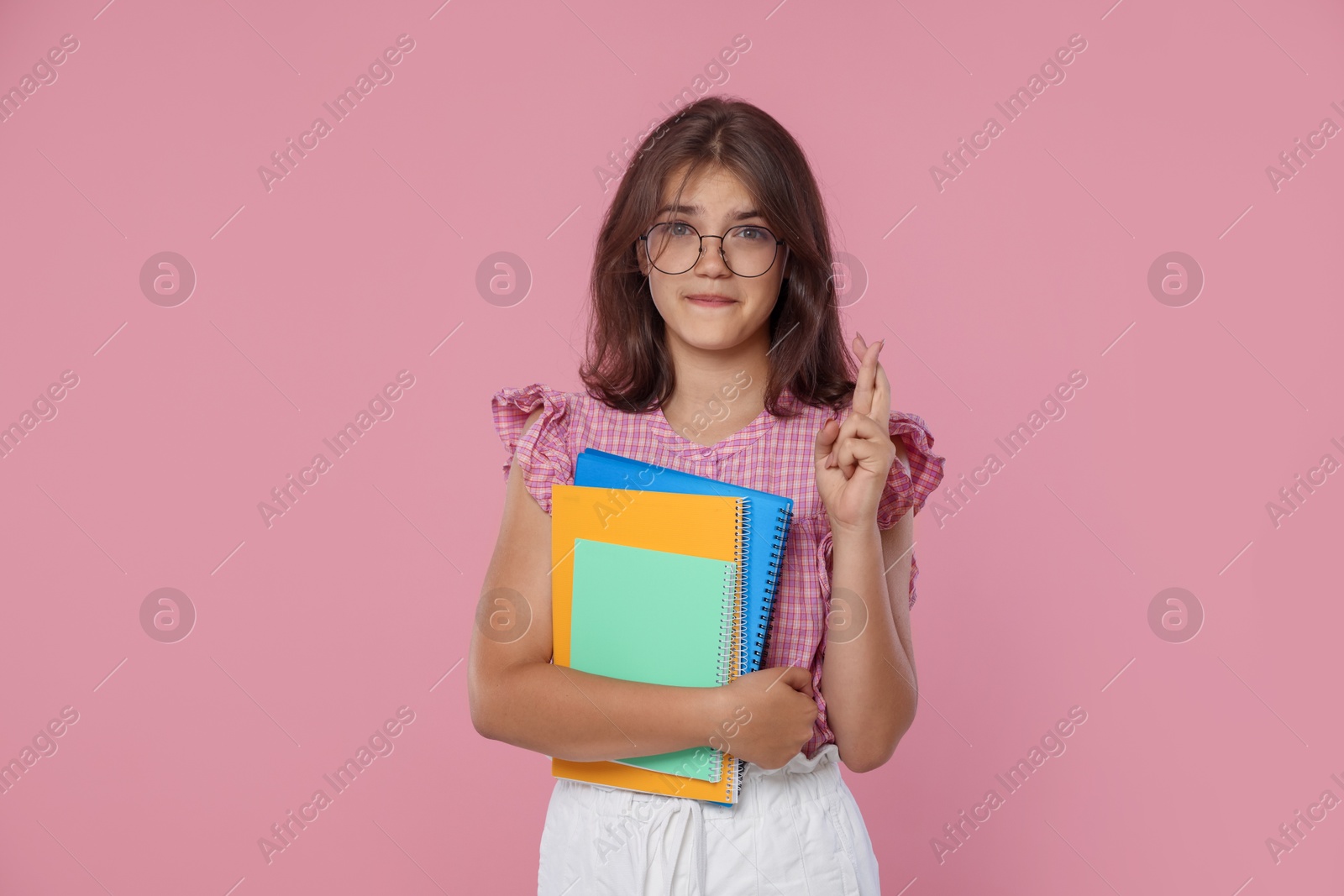Student with notebooks crossing fingers on pink background. Hope for good exam result Photo of Student with notebooks crossing fingers on pink background. Hope for good exam result