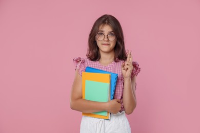 Photo of Student with notebooks crossing fingers on pink background. Hope for good exam result
