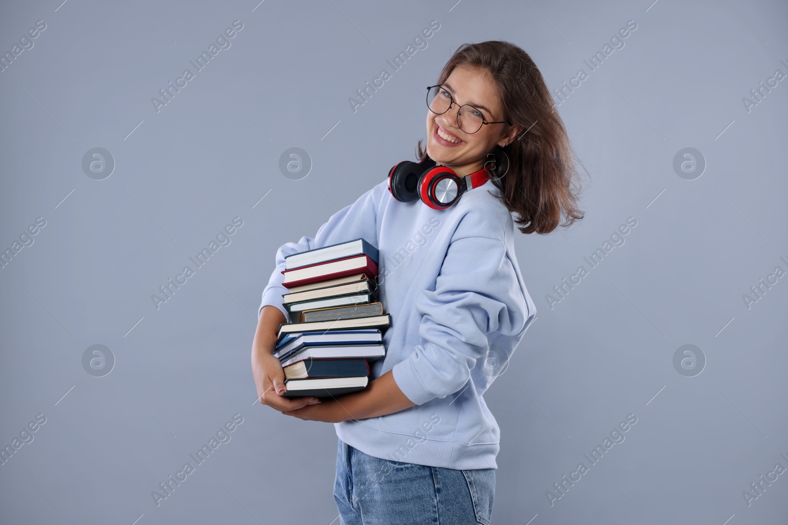 Student with stack of books feeling happy about her good exam result on gray background Photo of Student with stack of books feeling happy about her good exam result on gray background