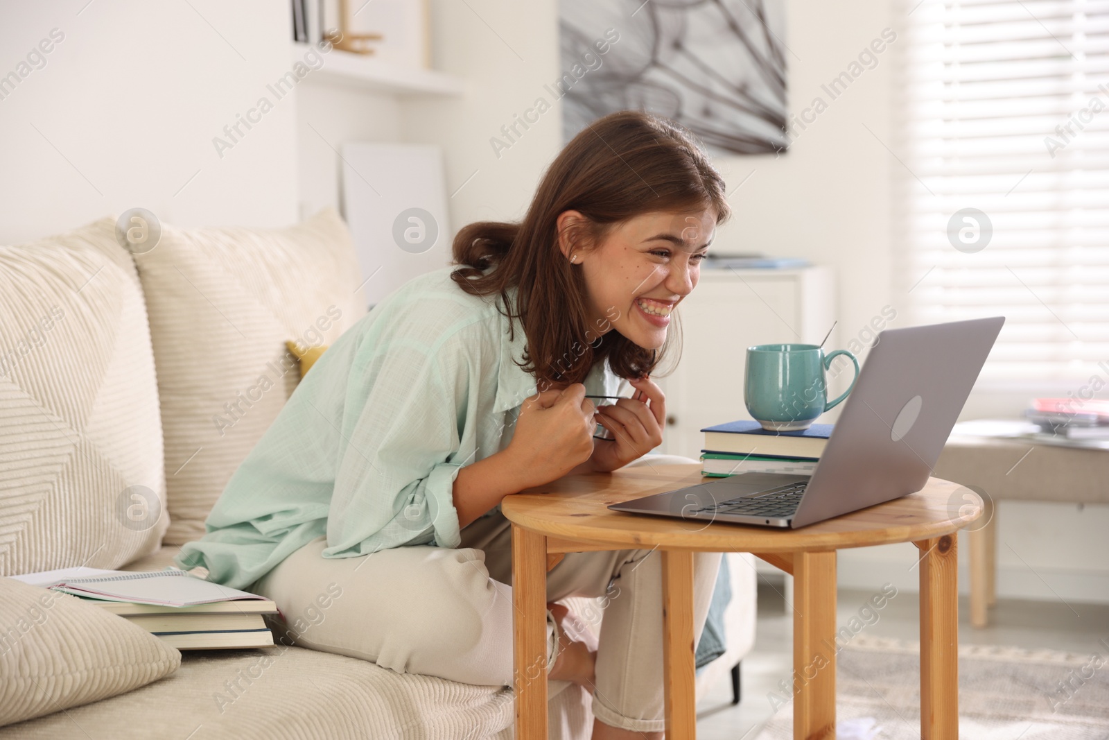 Student feeling happy about her good exam result at wooden table with laptop indoors Photo of Student feeling happy about her good exam result at wooden table with laptop indoors