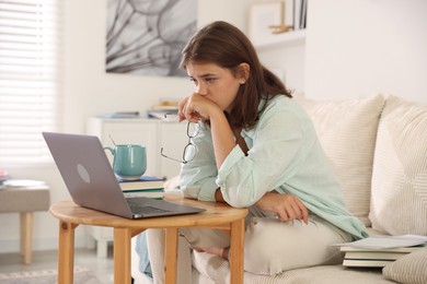 Photo of Student feeling unhappy about her exam result at wooden table with laptop indoors