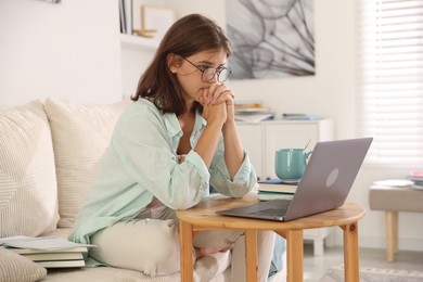 Photo of Student feeling unhappy about her exam result at wooden table with laptop indoors