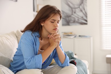 Photo of Student praying for good exam result on sofa indoors