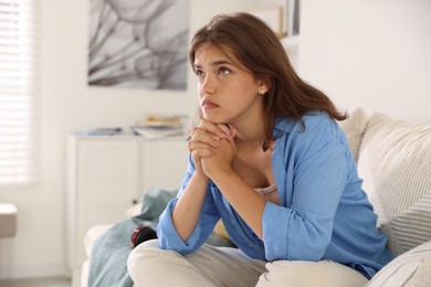 Photo of Student praying for good exam result on sofa indoors
