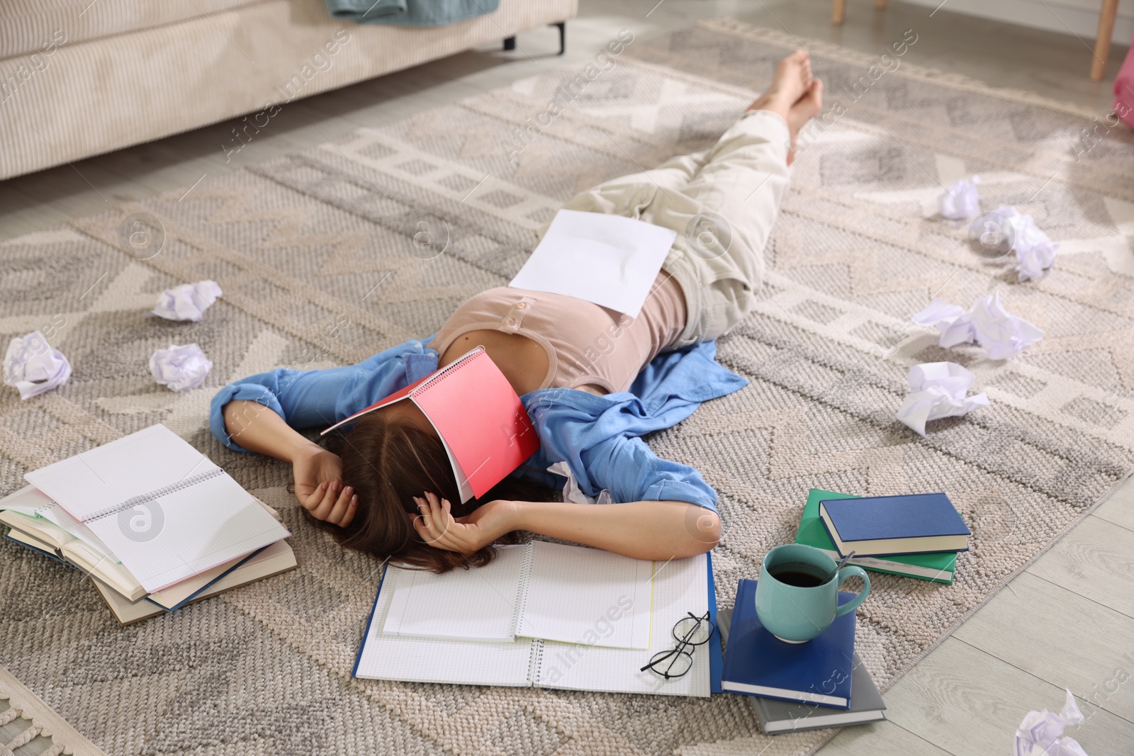 Tired teenage student among notebooks, crumpled paper and coffee on rug indoors. Preparing for exam Photo of Tired teenage student among notebooks, crumpled paper and coffee on rug indoors. Preparing for exam