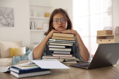 Photo of Tired student with stack of books preparing for exam at table indoors